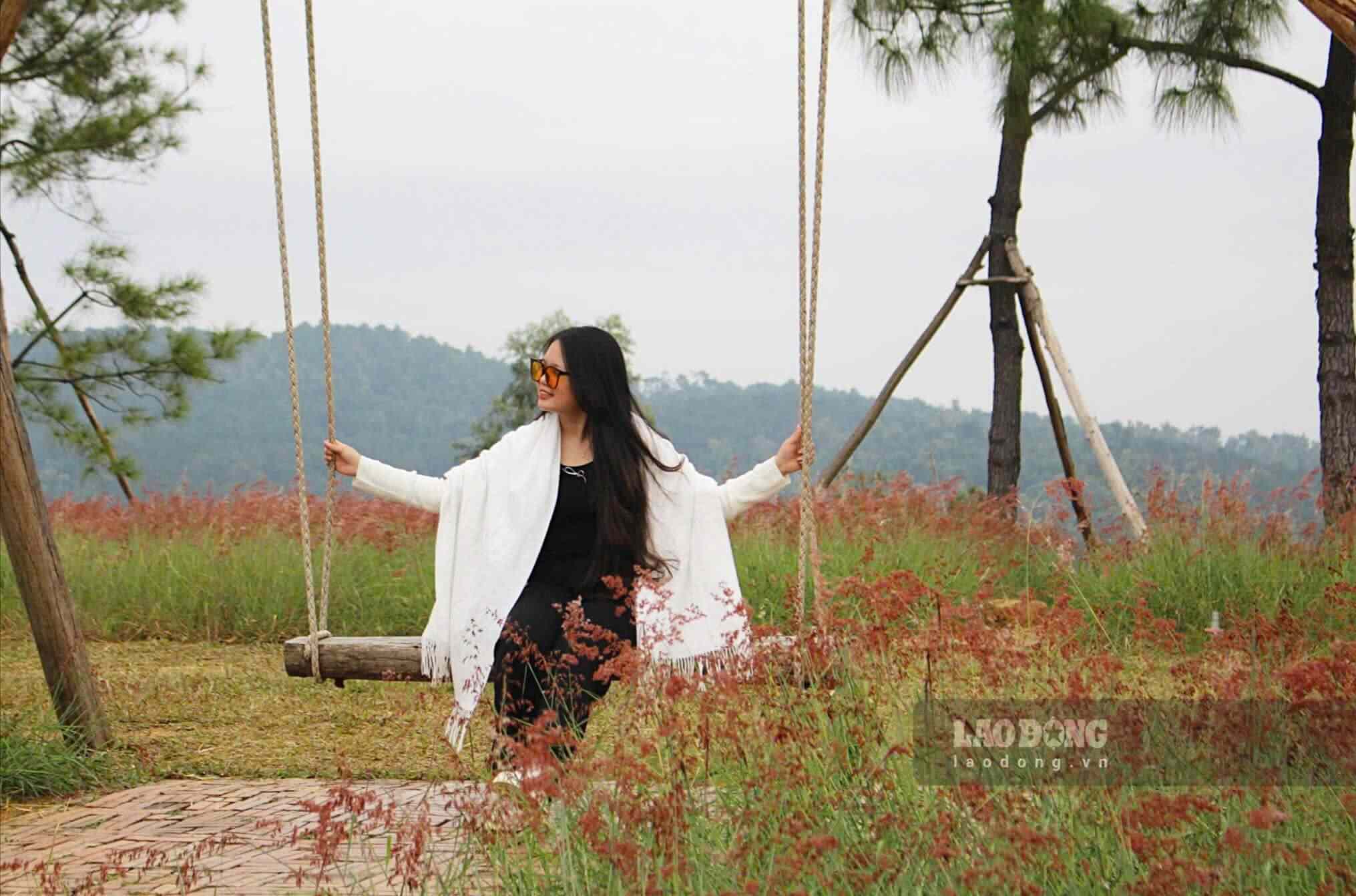 A área gramada da colina está decorada com miniaturas como cabanas, cadeiras, balanços, etc., para atender às necessidades dos turistas que desejam tirar fotos. O ar na colina de grama rosa é fresco e agradável. Do alto da colina, entre os tufos de grama rosa que brilham como seda fina sob a luz do sol, os turistas podem admirar a paisagem da vila, com a fumaça flutuando ao longe, criando uma beleza pacífica e tranquila.