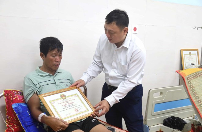 El presidente del Comite Popular de la Zona Especial de Ly Son Quang Ngai entrega certificados de merito al Sr. Phan Duy Quang por su valiente acto de rescate de personas en la tormenta numero 13. Foto: Nguyen Thanh