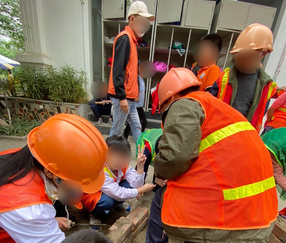 Tre em dang duoc nguoi lon huong dan de trai nghiem mot ngay lam cong nhan xay dung. Anh: Duc Van