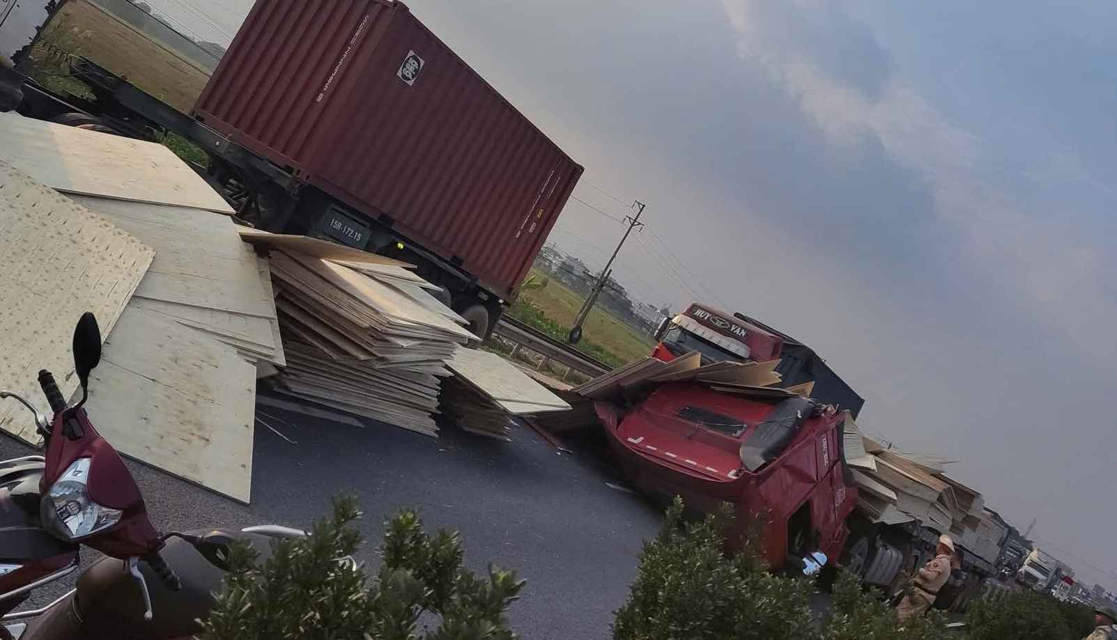 Hiện trường xe đầu kéo đổ gục phần đầu, gỗ vương vãi khắp mặt đường.