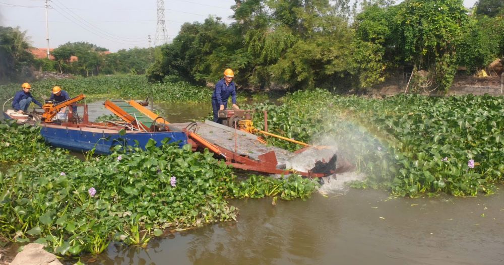 Ông Kim và các cộng sự vận hành máy chém vớt bèo trên sông.