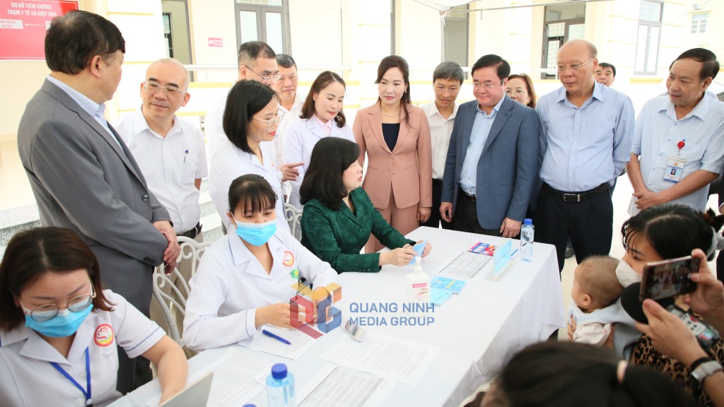 Minister Dao Hong Lan checks the vaccination books at the area welcoming children to get vaccinated against measles at Hiep Hoa Commune Health Station, Quang Yen Town. Photo: Quang Ninh Provincial Media Center