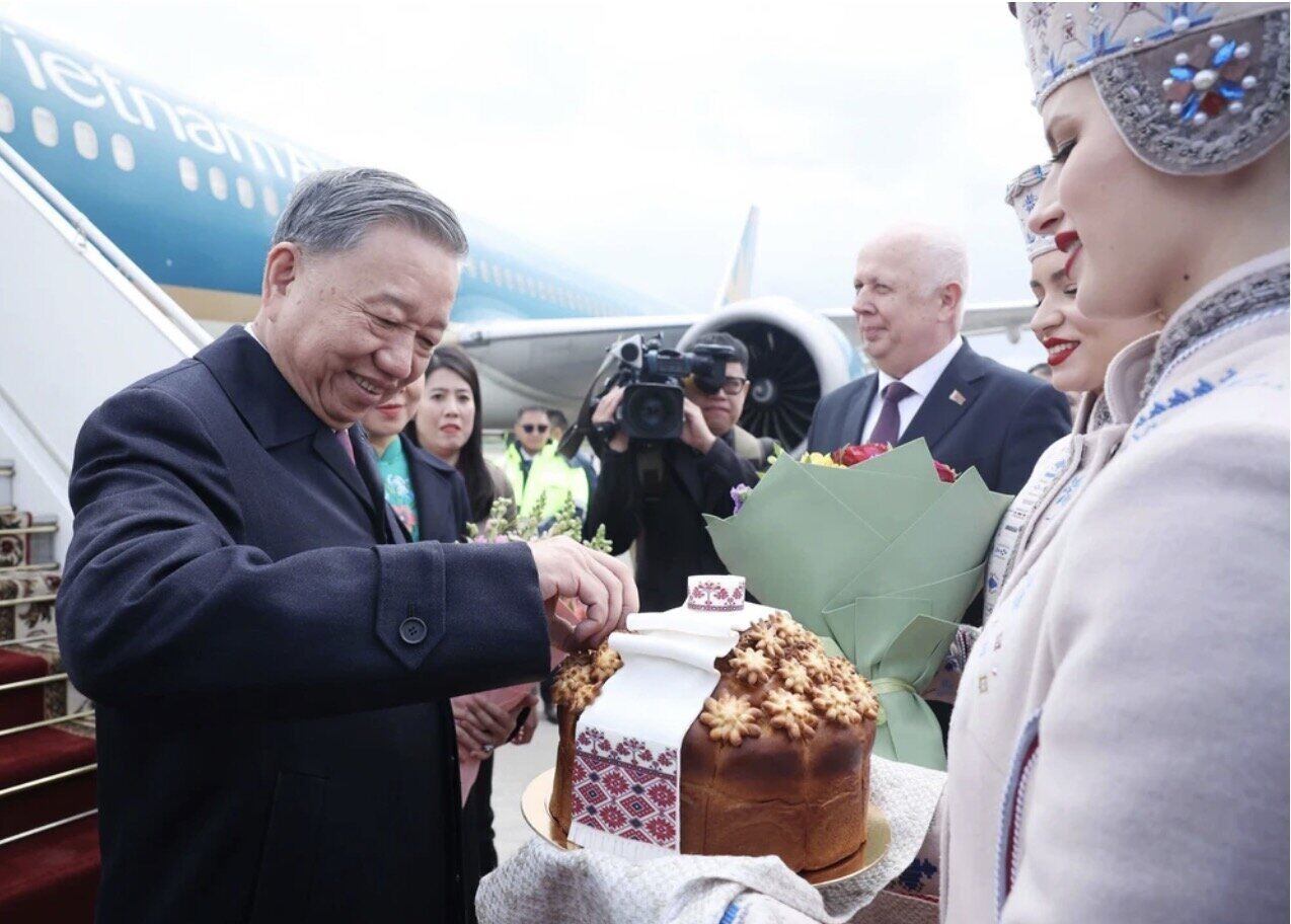 Thiếu nữ Belarus trong trang phục truyền thống trân trọng mời Tổng Bí thư Tô Lâm thưởng thức bánh mì và muối theo nghi thức đón khách quý của Belarus. Ảnh: TTXVN 
