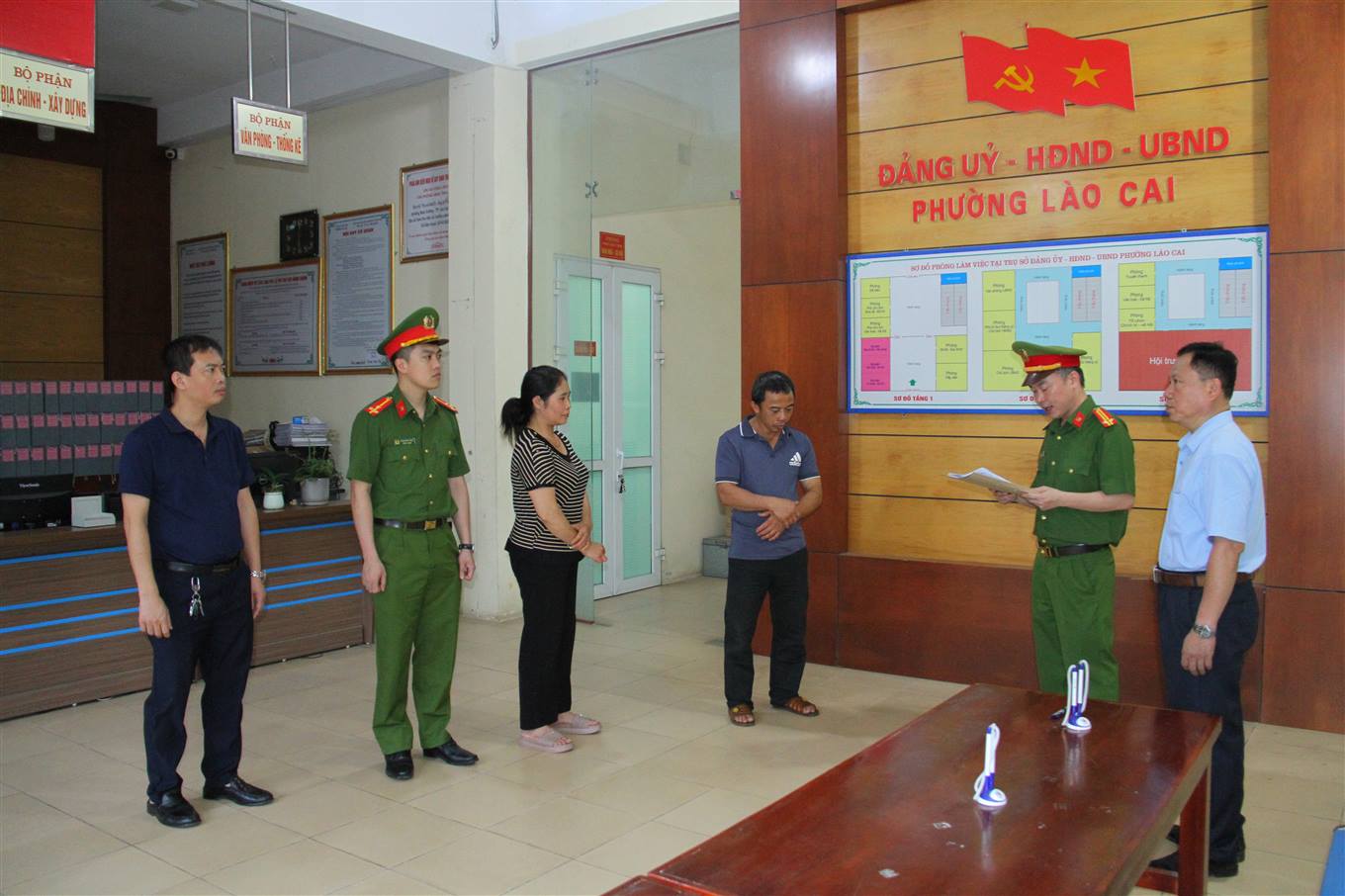 Công an đọc quyết định khởi tố Tạ Văn Hải và Lê Thị Thắm (chắp tay phía trước). Ảnh: Công an cung cấp

