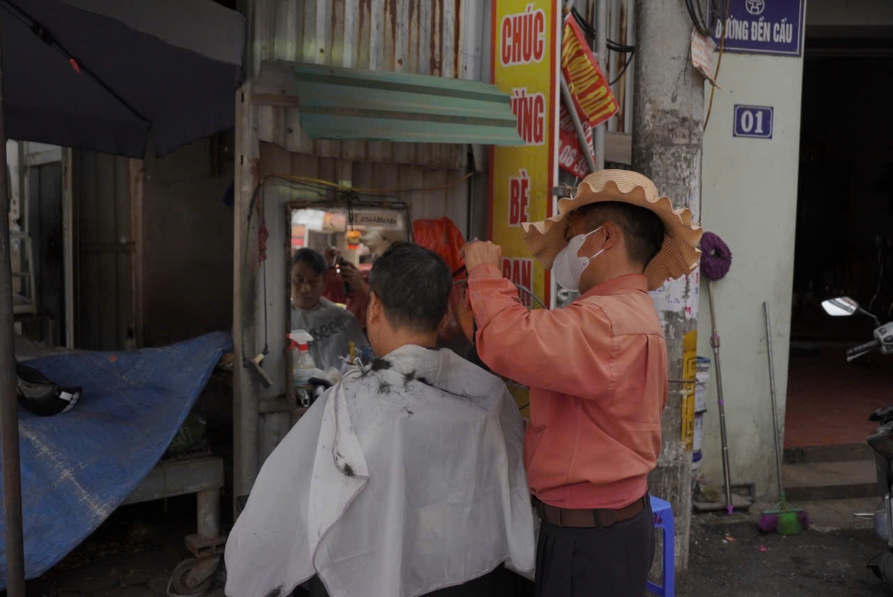 Ong Nguyen Van Tu cat toc cho khach tai nga 3 Van Trai, xa Van Phu (huyen Thuong Tin, Ha Noi) dung cat toc cho khach trong tinh trang ca chu ca khach deu nhan nho vi nang nong. Anh: Phuong Anh
