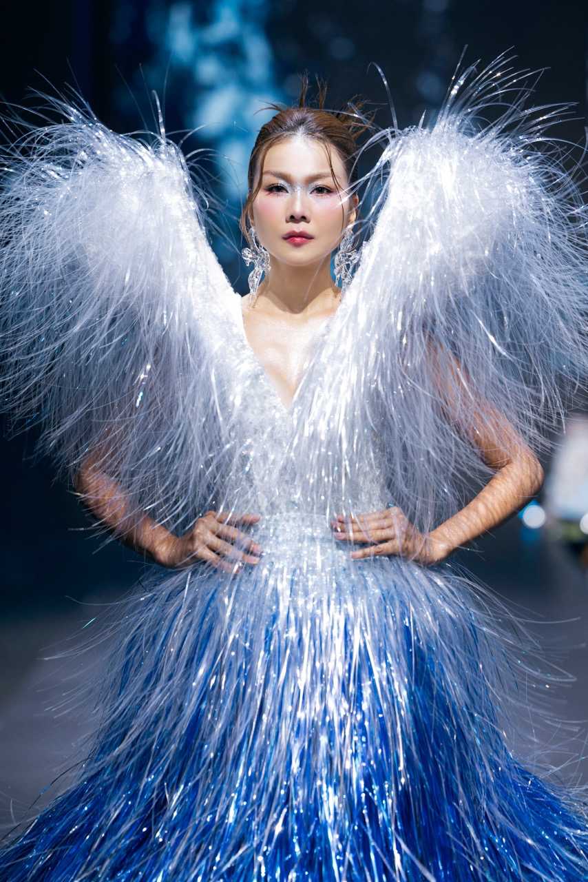 Bo vay tao hinh nhu mot dai song anh sang song dong, voi phan than vay phu kin bang chat lieu soi anh kim tong bac - xanh navy ombre, chuyen sac tua nhu mat nuoc phan chieu anh sang trong dem.