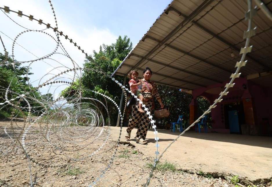 Mot phu nu be tre di ngang qua day thep gai ma Campuchia to Thai Lan dat tai tinh Banteay Meanchey, ngay 14.8.2025. Anh: Xinhua