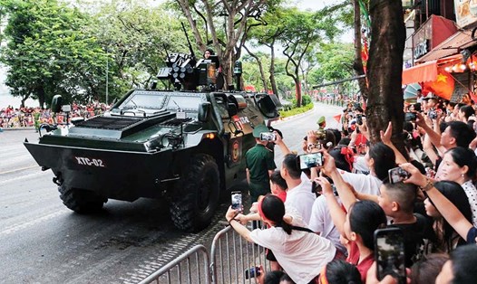 Người dân vẫy chào xe thiết giáp chở quân XTC-02 đi qua đường Thanh Niên về điểm tập kết, sẵn sàng tham gia buổi tổng hợp luyện tối 24.8. Ảnh: Tô Thế