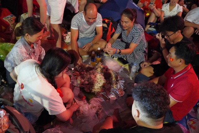 Bua com gia dinh am cung, vui ve voi xoi nep, ga luoc cua mot gia dinh den tu Ba Vi, Ha Noi. Dieu dac biet la bua com nay dien ra ngay tren he pho, xung quanh la bien nguoi dang cho doi cuoc tong duyet dieu binh dieu hanh dien ra ngay mai. Anh: Pham Duc