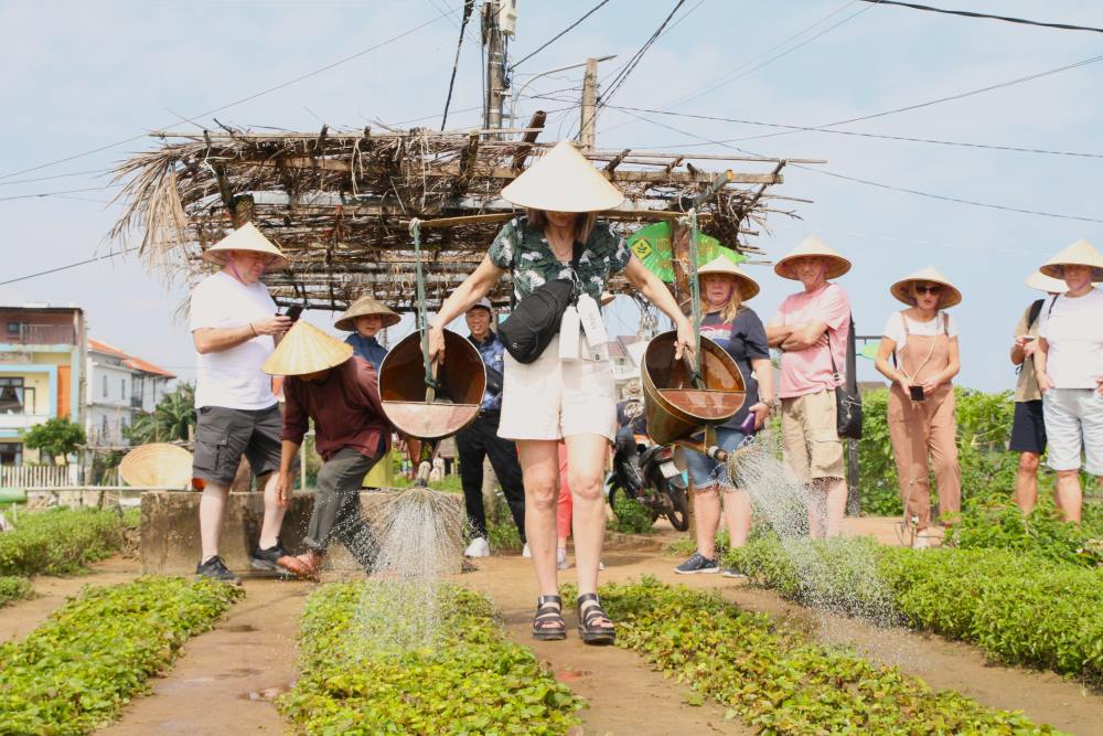 Foreign tourists excitedly carry a load of watering vegetables at Tra Que vegetable village, Da Nang. Photo: Thanh Huyen