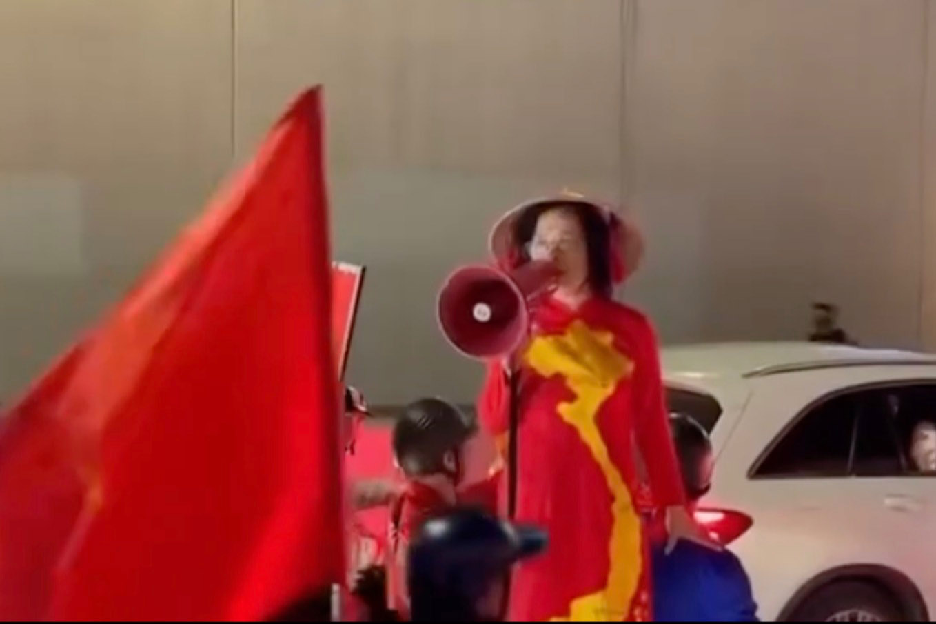 Bà T đứng lên yên xe máy, cầm loa hô hào người dân đua xe sau trận thắng của U23 Việt Nam trước U23 UAE. Ảnh: Cắt từ clip 
