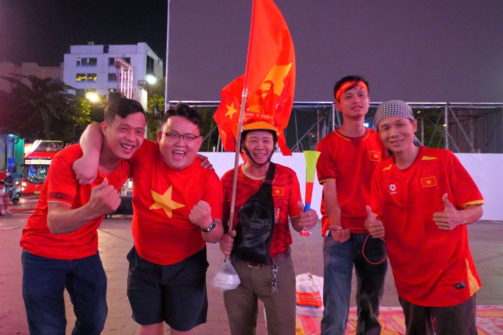 Mot nhom ban tre voi bang ron “Viet Nam Chien Thang” dang check-in som truoc man hinh LED lon.