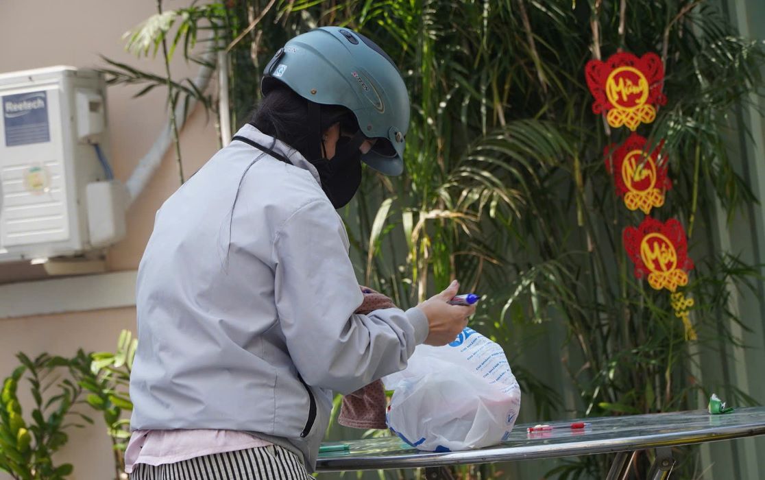 Chị Chi dùng bút, viết tên, lớp của con để cô giáo mang vào trường. Ảnh: Chân Phúc