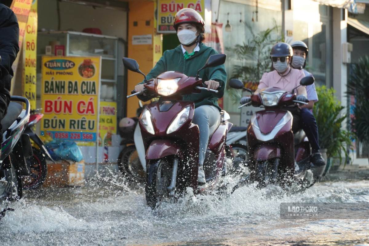 Người dân chật vật điều khiển xe máy qua những đoạn đường ngập nước do triều cường dâng cao. Ảnh: Bảo Linh