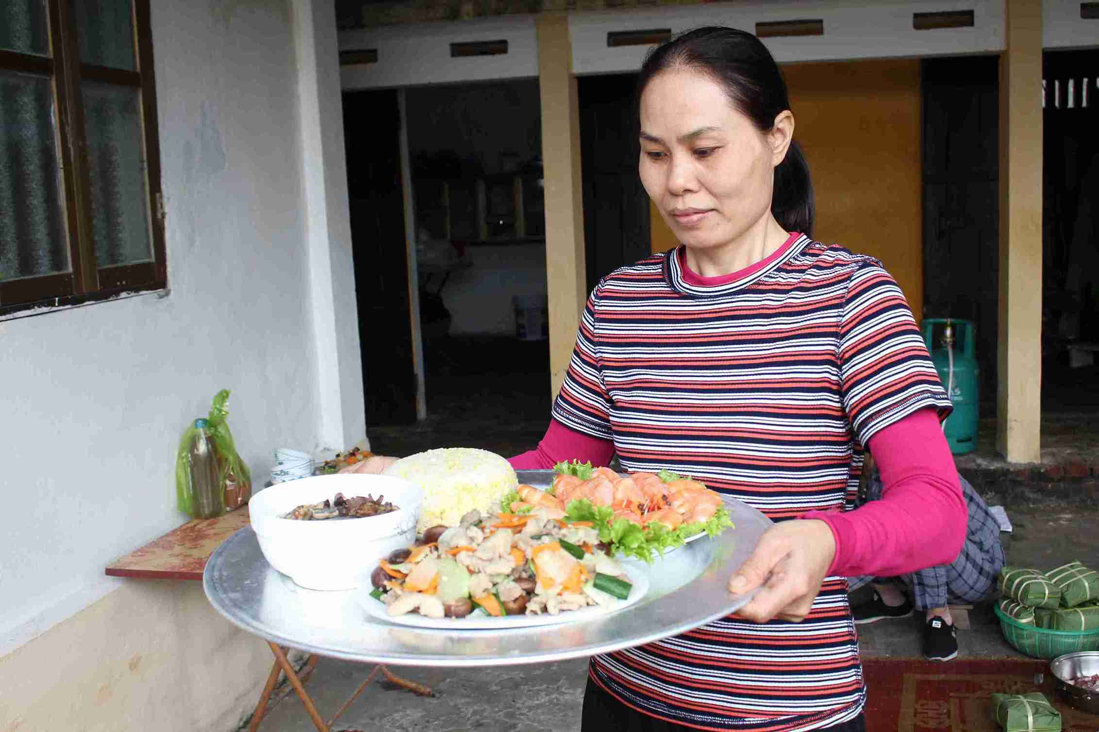 Chị Đào Thị Thinh bưng mâm cơm tất niên trong ngày gia đình sum họp.