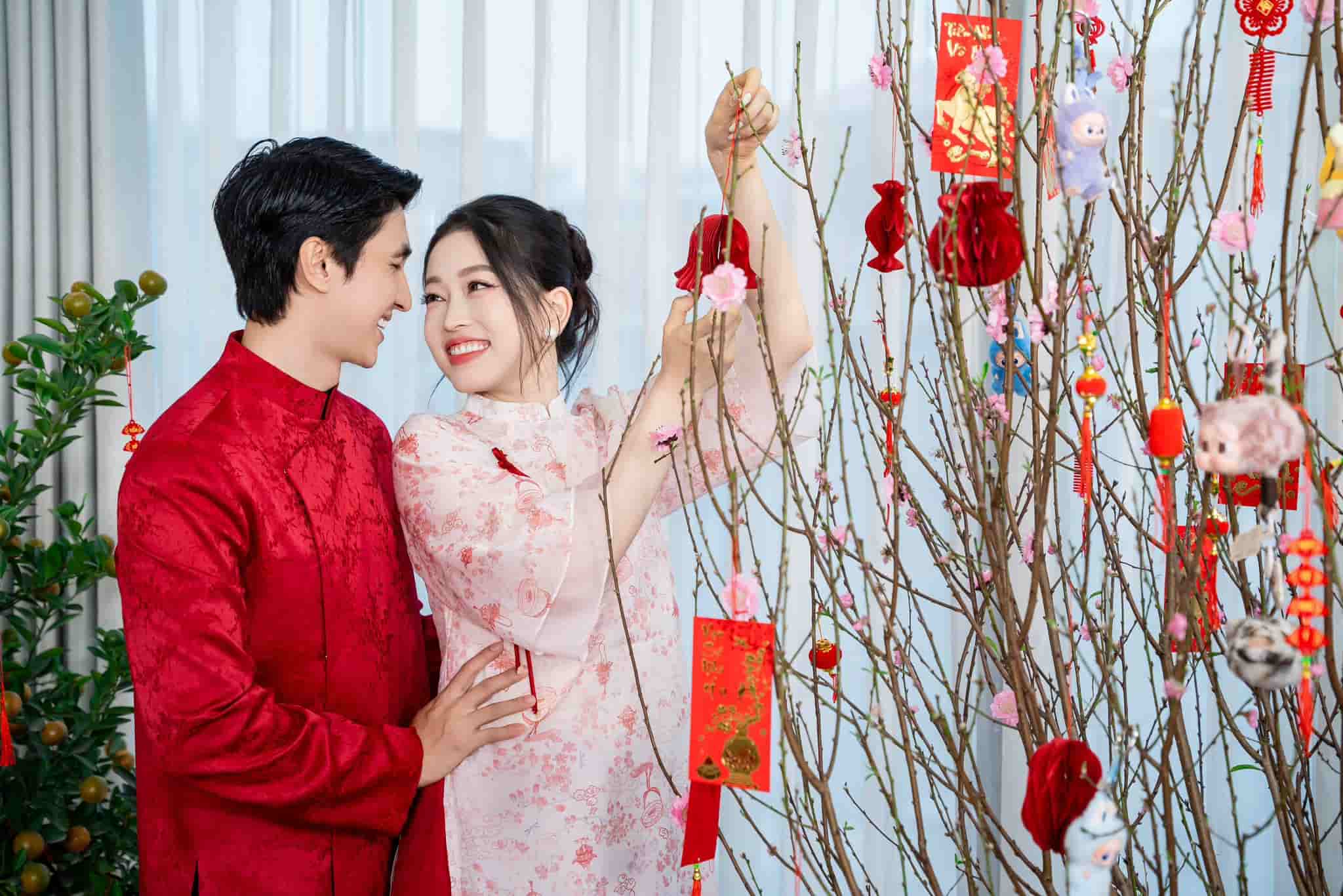 Vợ chồng diễn viên Bình An - Á hậu Phương Nga diện trang phục áo dài truyền thống bên cành đào ngày xuân.