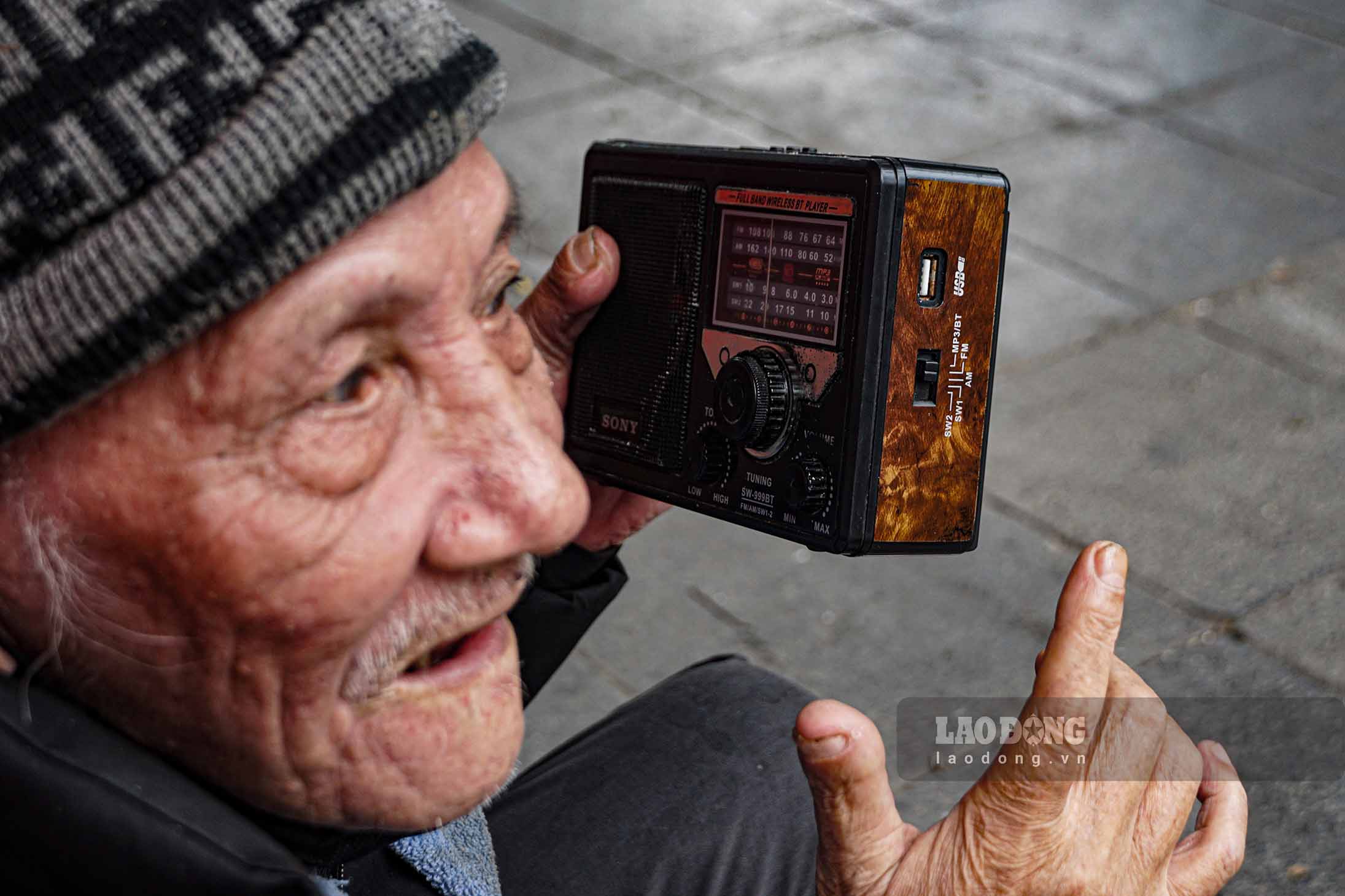 Một cụ ông ngồi nghe radio thư thái trên vỉa hè đường phố Hà Nội.