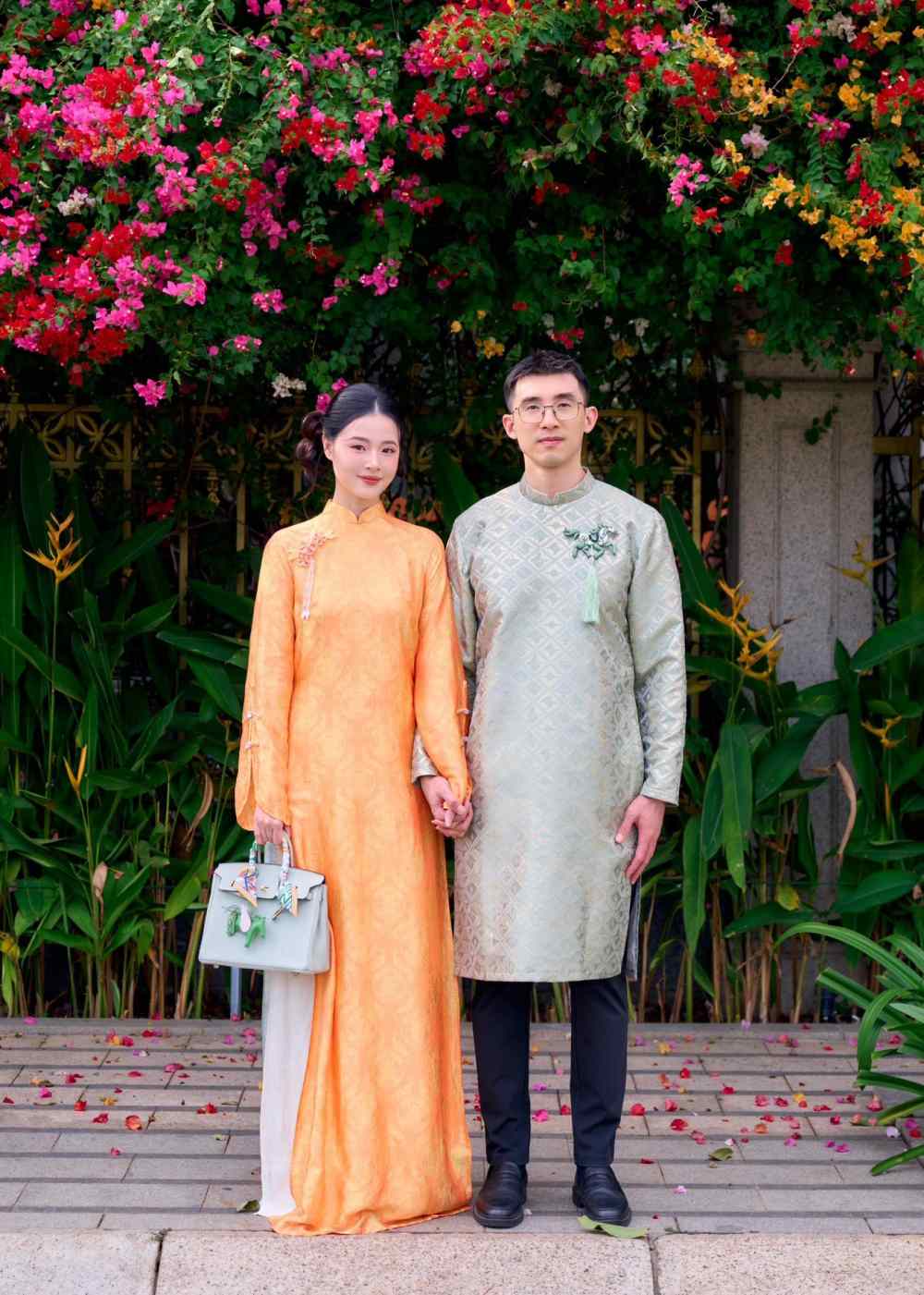 Midu cùng chồng du Xuân với áo dài màu cam nổi bật. Cô đeo túi Hermès hơn 600 triệu đồng chồng tặng. Ảnh: NVCC