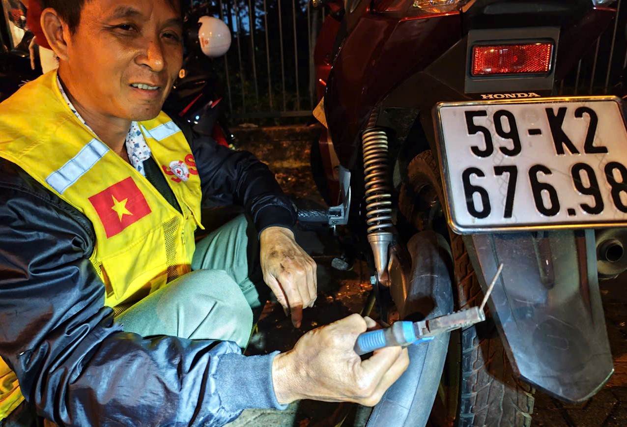 Tình nguyện SOS Bảo Lộc có mặt kiểm tra xe cho người dân gặp sự cố trên đường đi du xuân trong đêm tối trước khi vá xe miễn phí. Ảnh: Hải Đường 