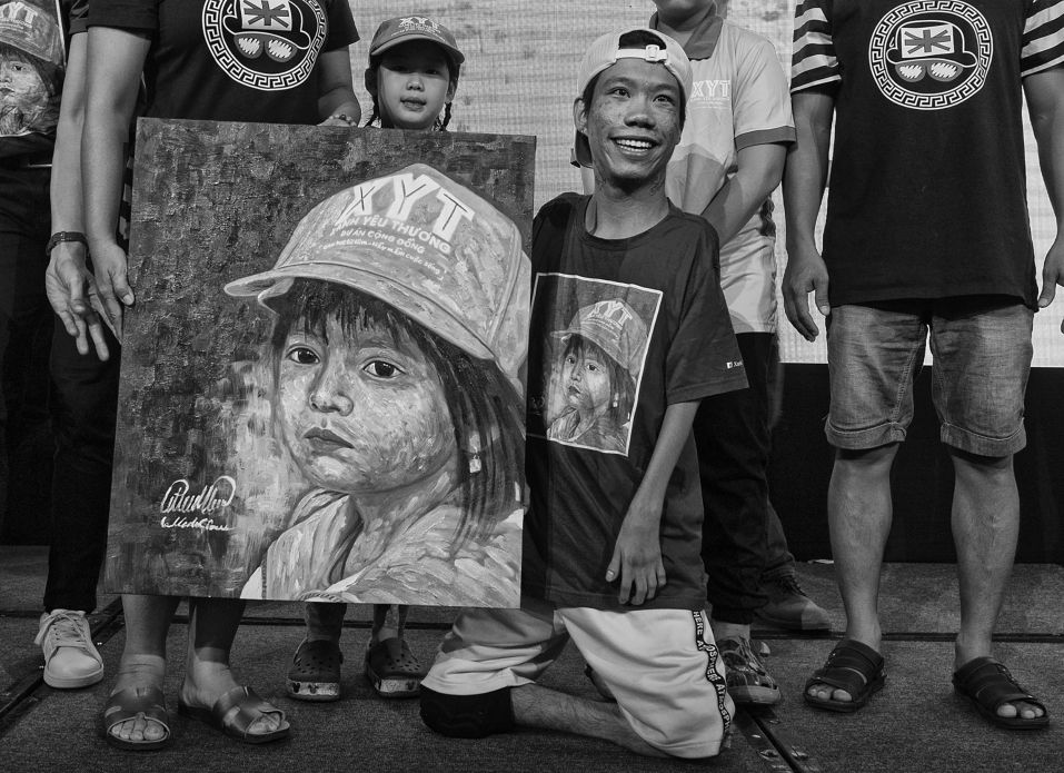 Họa sĩ Lê Minh Châu - nạn nhân chất độc màu da cam bên cạnh bức tranh anh vẽ làm từ thiện giúp trẻ em nghèo. Ảnh: Việt Văn