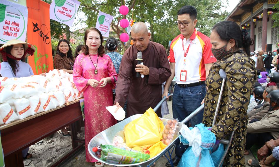 Người phụ nữ tàn tật được tình nguyện viên đẩy xe mua các mặt hàng ở chợ. Ảnh: Hưng Thơ