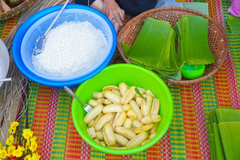 Không gian Tết xưa được dựng lại trước hiên nhà với bếp củi, nồi bánh tét đỏ lửa cùng những vật dụng quen thuộc như thúng nếp, rổ đậu xanh, dây lạt, lá chuối… tạo cảm giác gần gũi, mộc mạc. Tại đây, không khí chuẩn bị Tết diễn ra chậm rãi, ấm áp, khác hẳn với nhịp sống gấp gáp thường ngày.