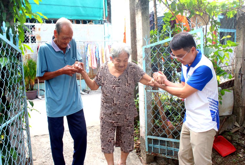 Ân cần dìu các cụ đến điểm sinh hoạt nhận quà. Ảnh: Lục Tùng