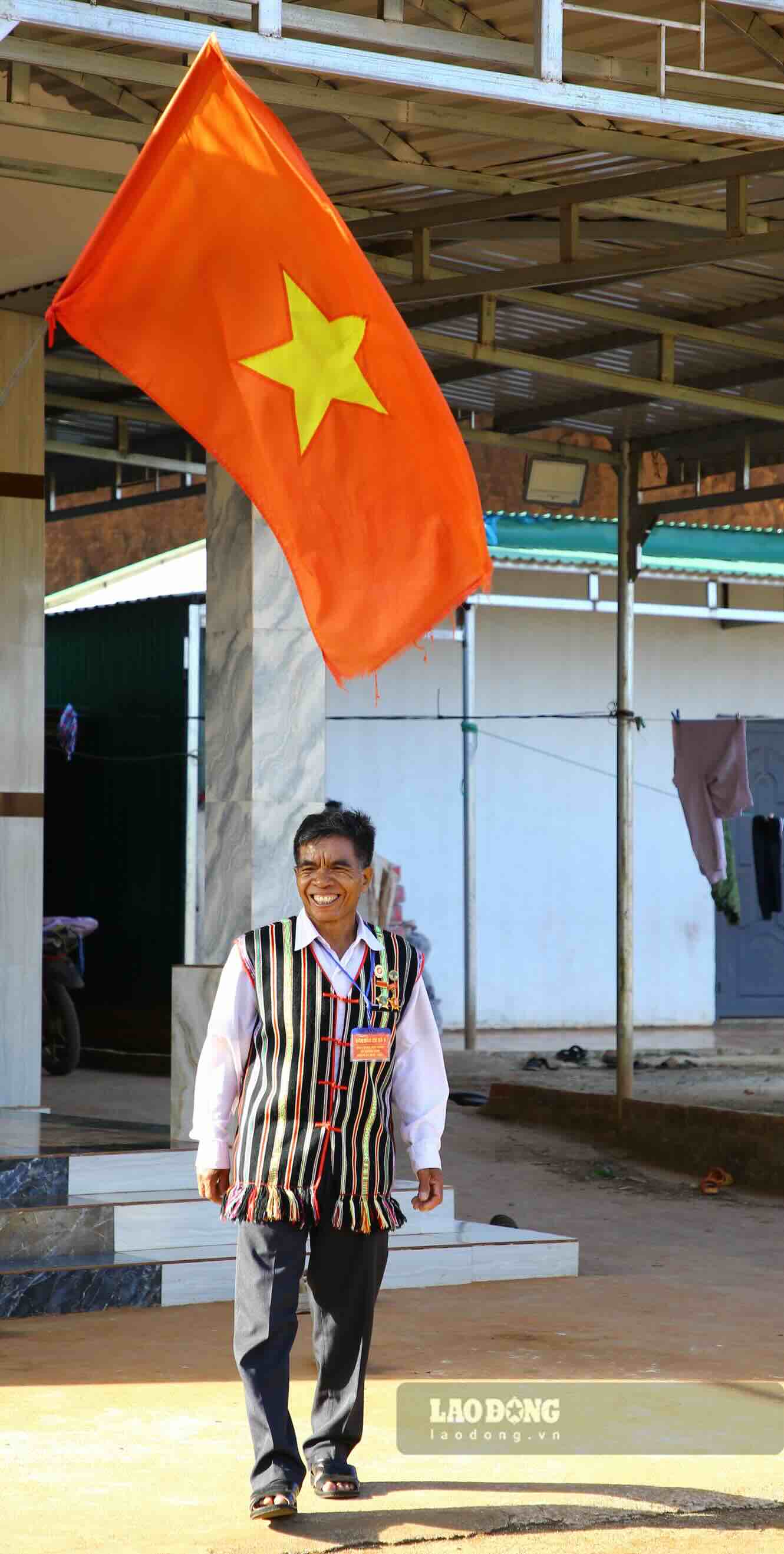 Dưới lá cờ Tổ quốc trước hiên nhà, già làng Điểu Sranh rạng rỡ lên đường đến nơi bỏ phiếu. Ảnh: Sáng Tuấn