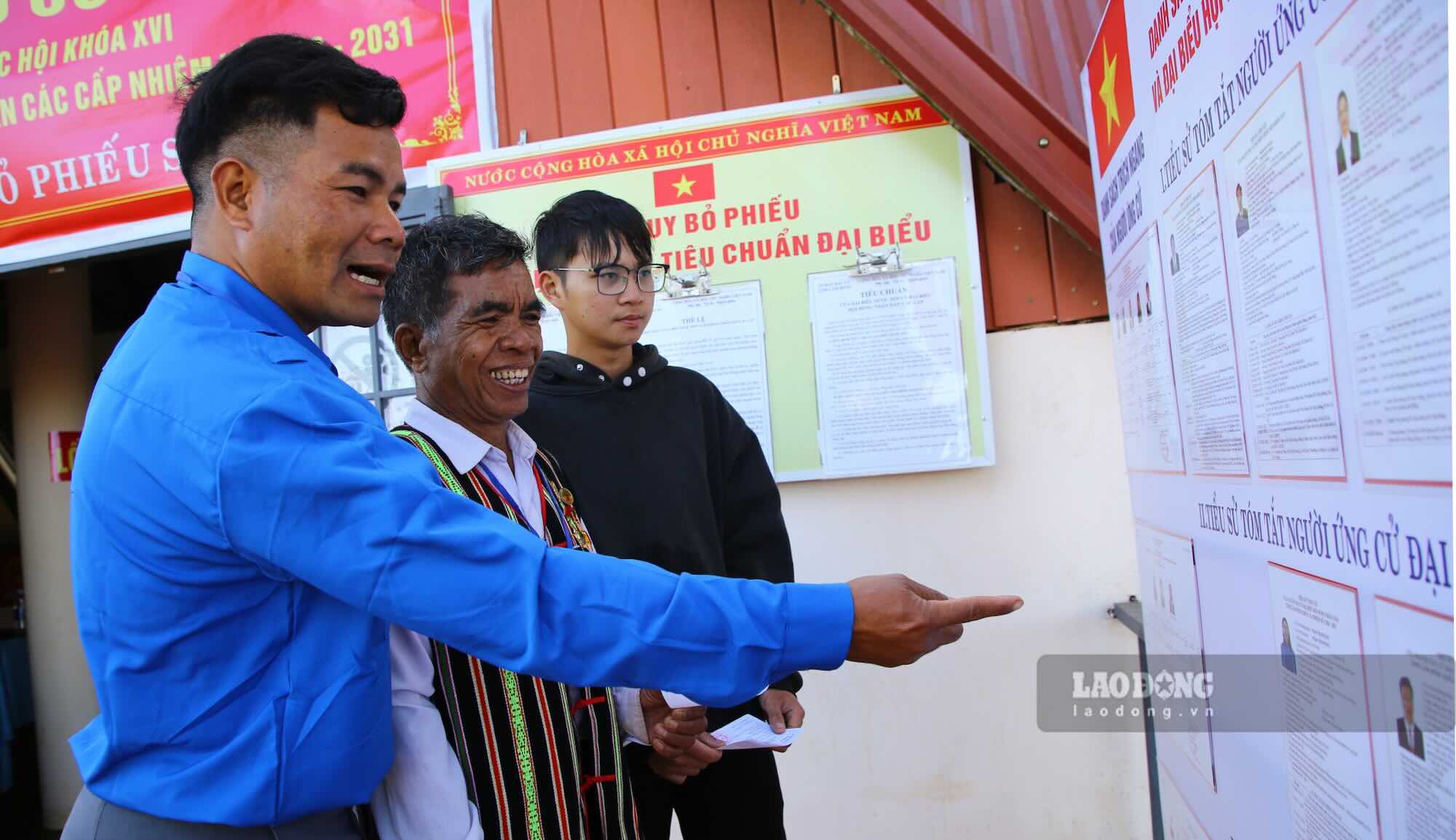 Tại điểm bầu cử, già làng Điểu Sranh được cán bộ hướng dẫn kiểm tra danh sách cử tri và nhận phiếu bầu. Ảnh: Sáng Tuấn