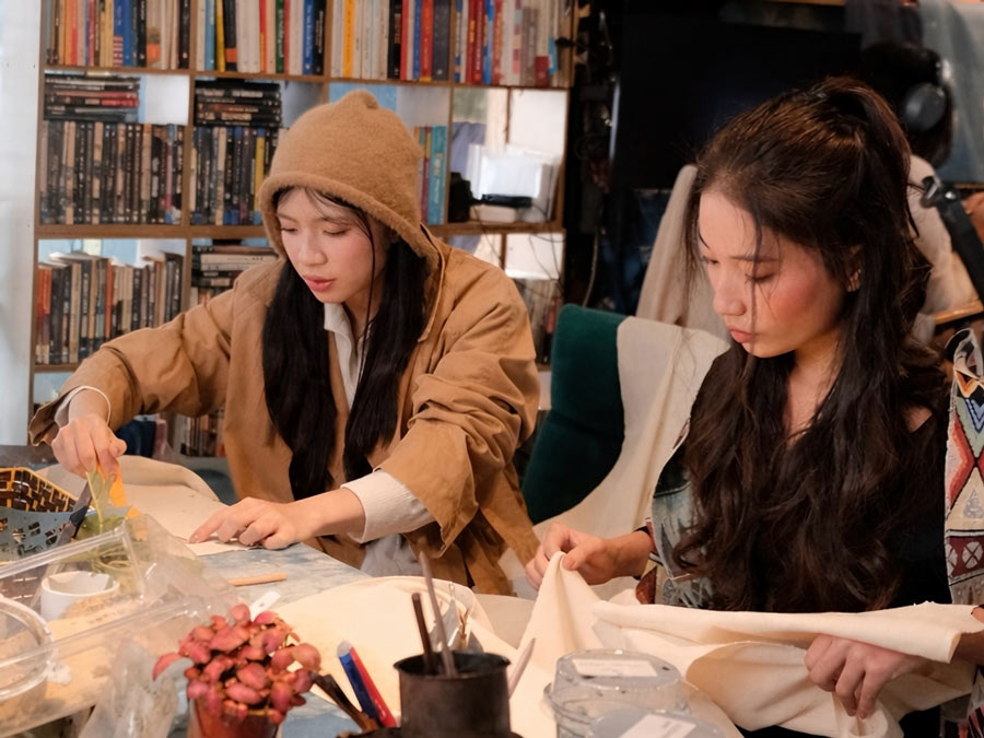 Bạn Nguyễn Quỳnh Anh (bên trái) trải nghiệm công đoạn tạo hình hoa văn bằng hỗn hợp hồ dán được nấu từ bột gạo nếp và cám gạo tẻ. Ảnh: Ánh Dương 