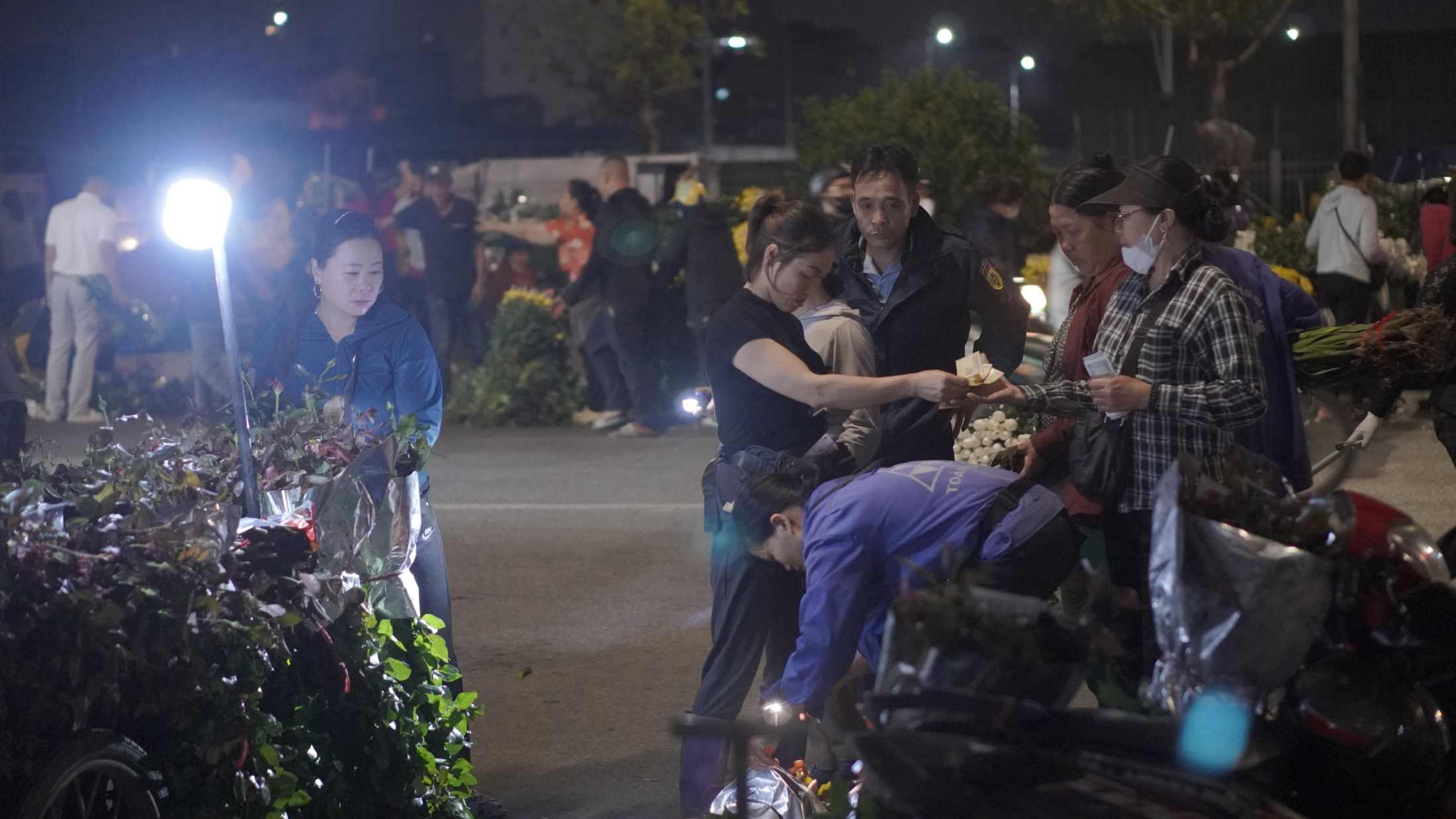 Tiểu thương tất bật mặc cả từng bó hoa dưới ánh đèn vàng giữa đêm Rằm tháng Giêng. Ảnh: Minh Vũ 