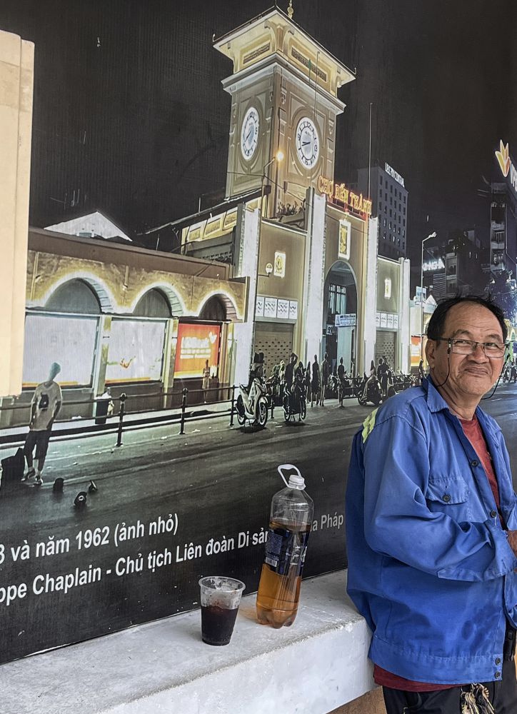 Người đàn ông tựa lưng bên bức ảnh chợ Bến Thành xưa và nay với ly cà phê đá còn dang dở. Ảnh: Việt Văn