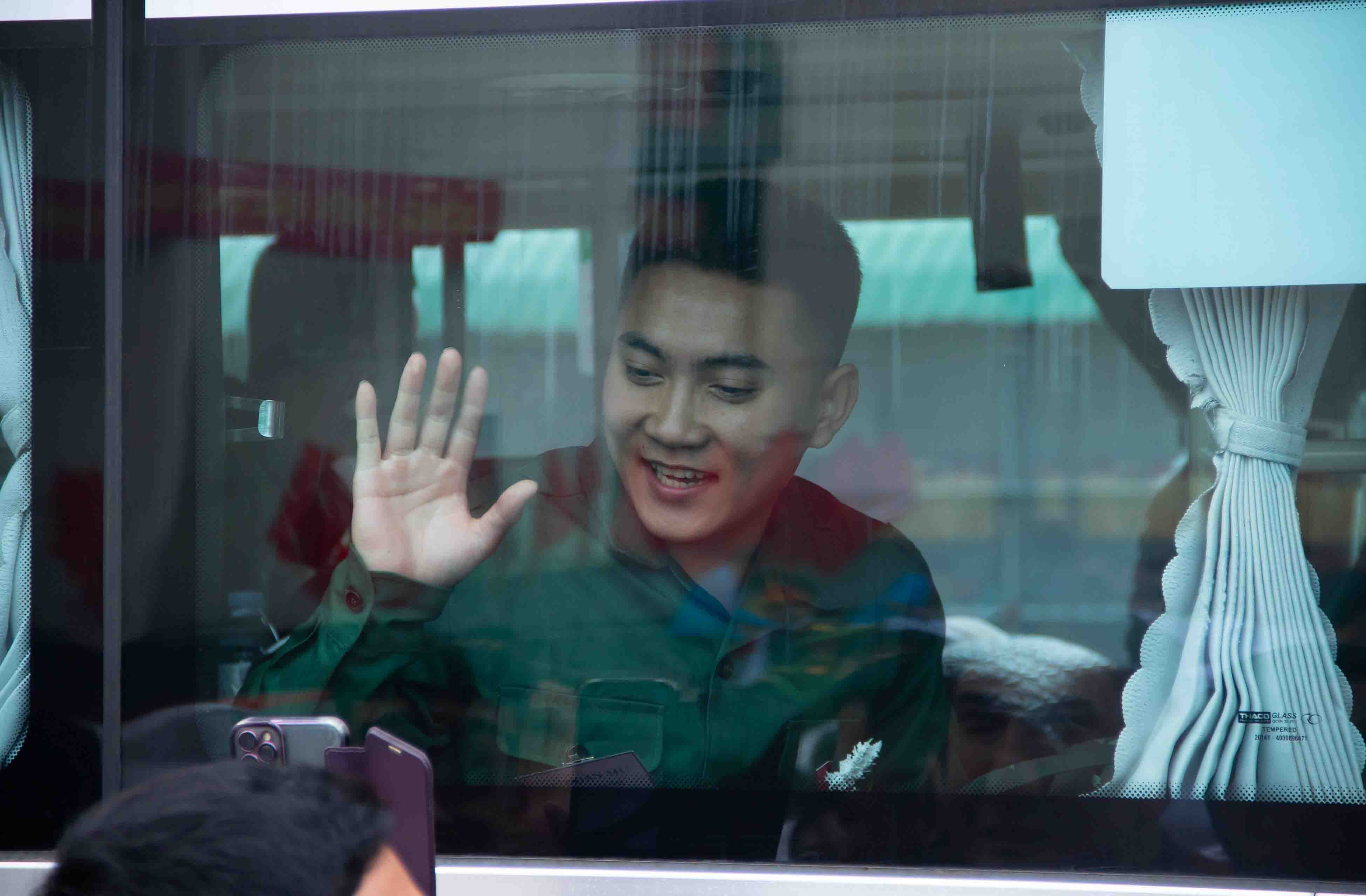 Một thanh niên nhập ngũ vẫy tay từ trong xe buýt, với nụ cười tươi và ánh mắt đầy hy vọng, trước khi lên đường thực hiện nghĩa vụ quân sự. Ảnh: Duy Chương