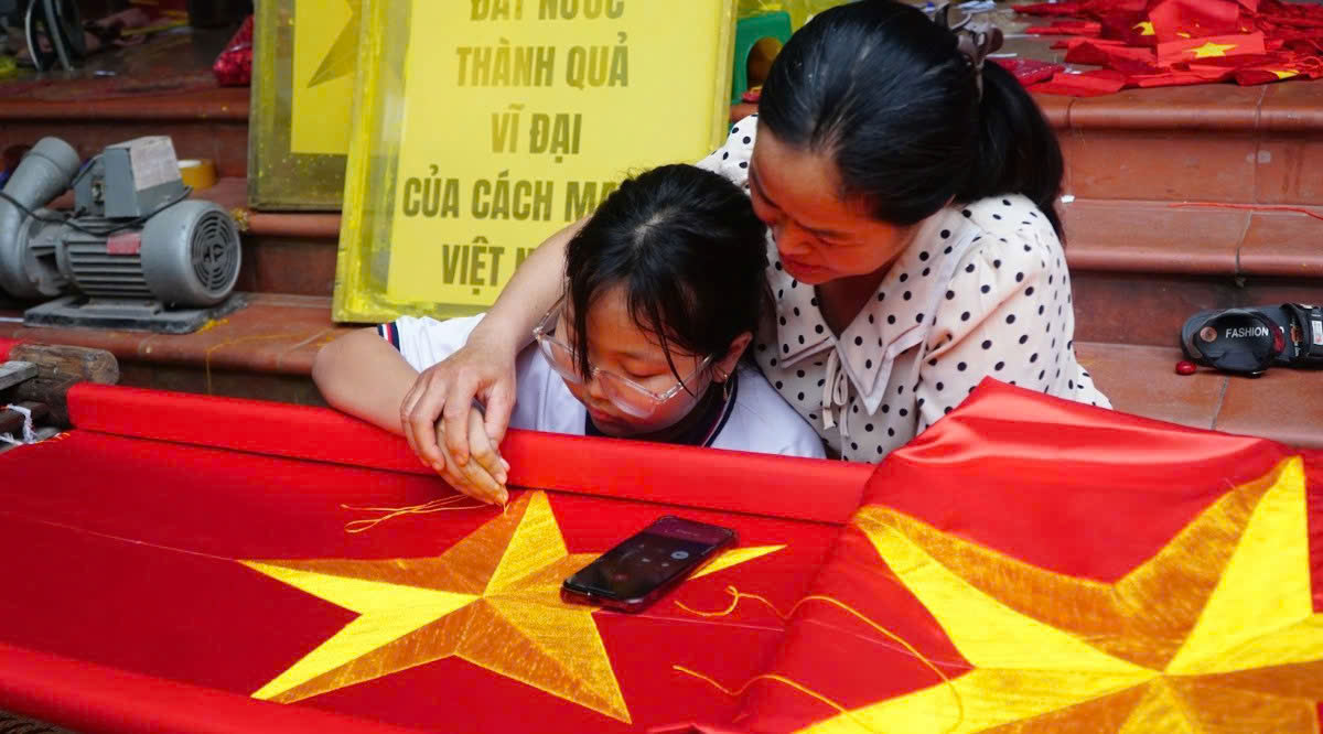 Chị Nhung truyền nghề thêu cờ cho thế hệ sau. Ảnh: Thanh Hằng