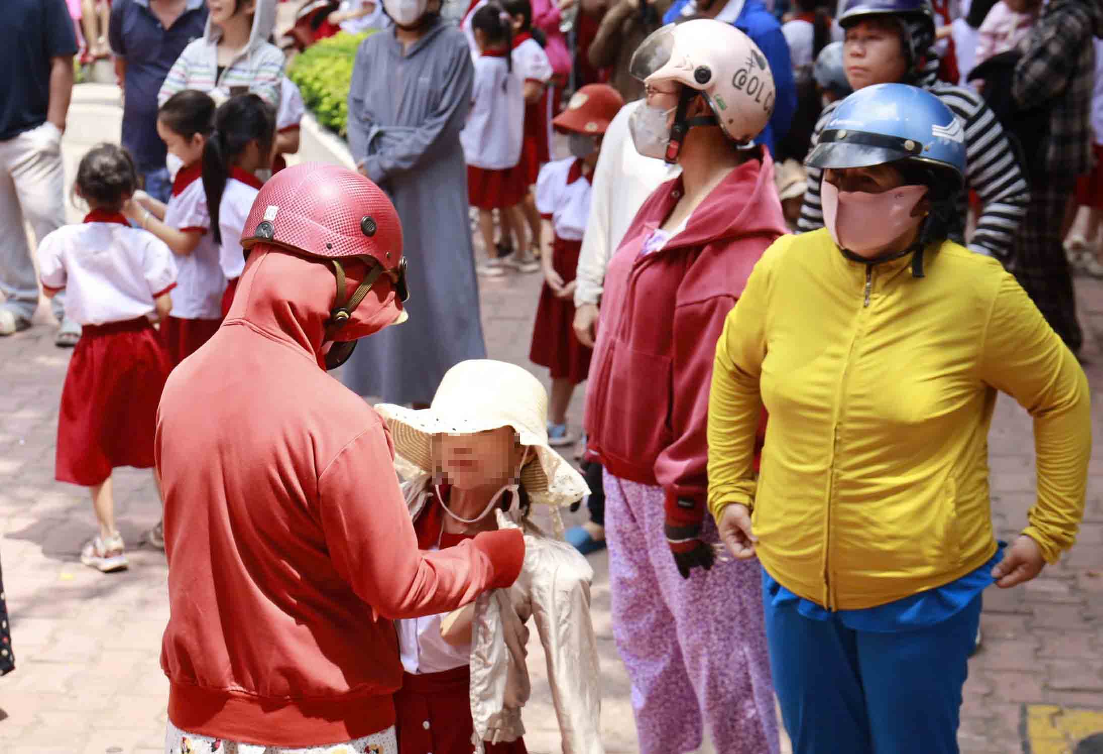 Phụ huynh che nắng, mặc áo cho con khi đưa đón học sinh giữa trưa nắng gắt. Ảnh: Minh Nguyễn