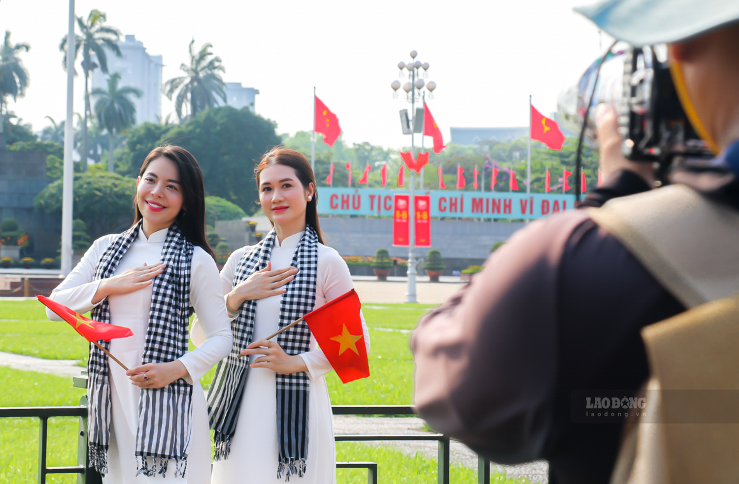 Trong nắng đầu hè của Hà Nội, hình ảnh các bạn trẻ trong tà áo dài, sơ mi trắng hay trang phục mang sắc đỏ, tay cầm quốc kỳ, tạo nên bức tranh vừa trang nghiêm vừa rộn ràng giữa không gian lịch sử.