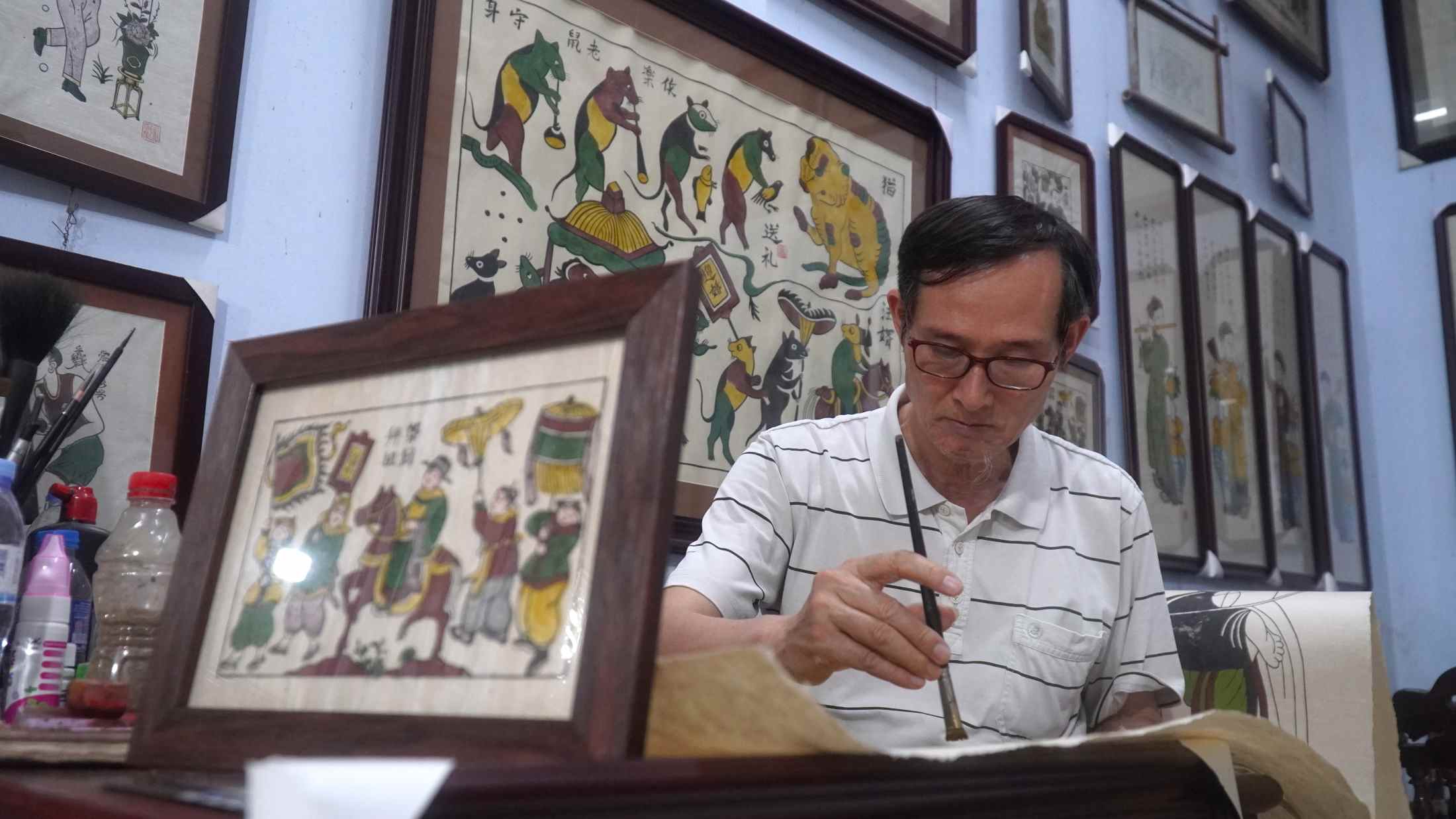 Trong không gian đậm chất làng nghề ấy, Nghệ nhân Ưu tú Nguyễn Hữu Quả lặng lẽ bên bàn in, tỉ mỉ chồng từng lớp màu tự nhiên lên những mộc bản gỗ đã nhuốm dấu thời gian.