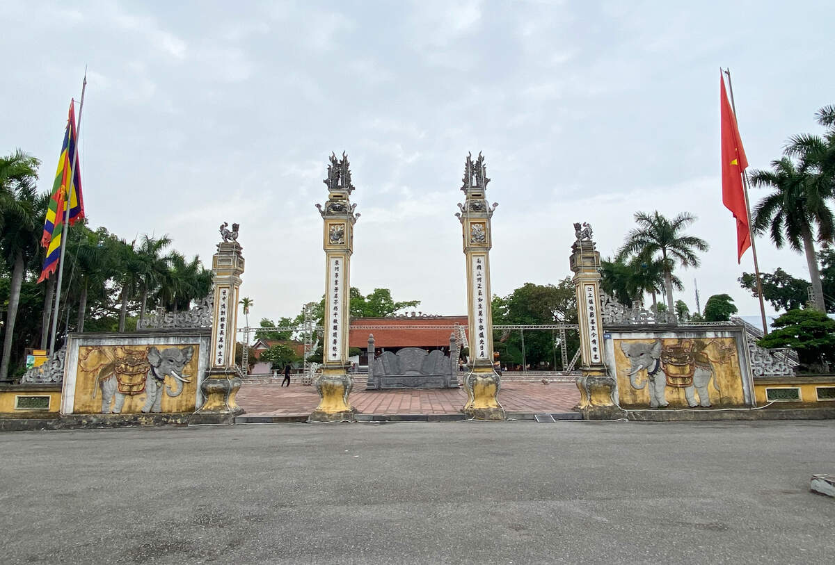 Cổng đền là nghi môn trụ biểu đồ sộ vút cao. Cổng giữa rộng 3,56m, hai cổng bên rộng 2,63m. Các trụ xây hình vuông, trên đầu hai trụ giữa đắp nổi phù điêu tứ long hạ. Hai trụ bên thấp hơn, đắp nổi nghê chầu. Cổ trụ đắp nổi nhiều hoạ tiết hoa văn trang trí. Tường hai bên cột trụ đắp nổi hình hai con voi và trang trí hoa văn hình kỷ hà. Trước nghi môn có đôi voi đá chầu, phủ phục. Thân cột trụ đắp nổi 4 đôi câu đối, nội dung ca ngợi Đức Thánh Trần. Ảnh: Nguyễn Huệ