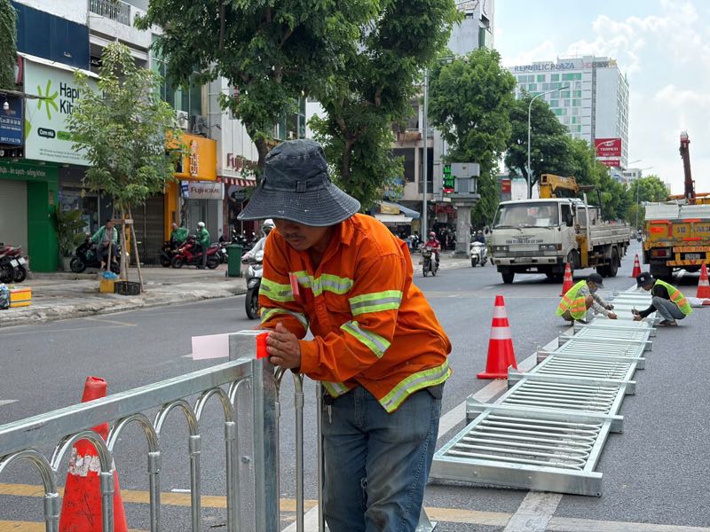 Nhóm công nhân dán băng keo phản quang lên hàng rào thép nhằm tăng khả năng nhận diện vào ban đêm. Ảnh: Anh Tú