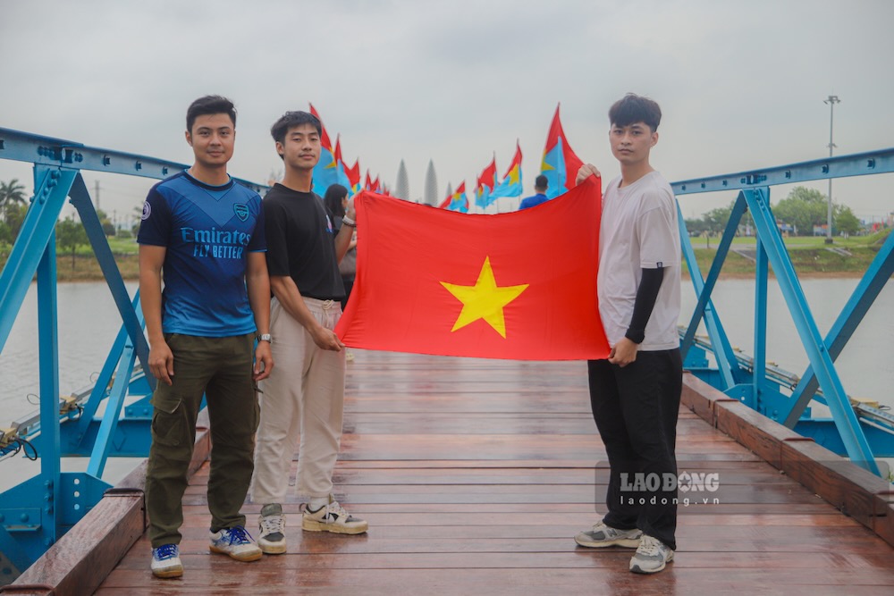 3 young men take pictures with the national flag at the Hien Luong - Ben Hai (Quang Tri province) Historical Relic. Photo: Nguyen Luan