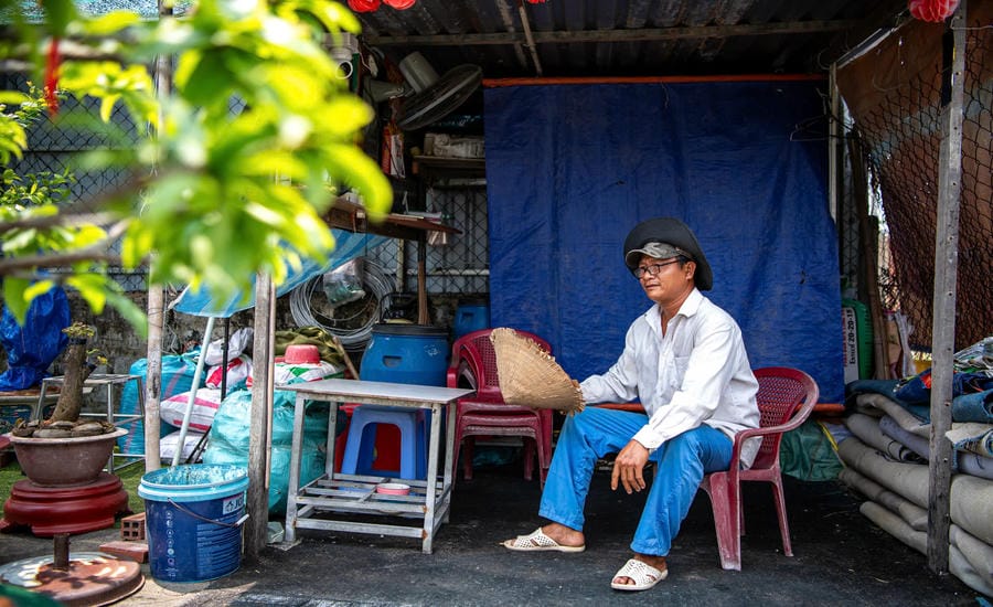 Dưới trời nắng gắt, ông Đình Tư (xã Bình Hưng) vừa quạt chiếc nón lá vừa chăm chú nhìn vườn cây cảnh. Vì thời tiết khắc nghiệt, ông phải ở lại vườn cả buổi trưa để tưới nước thường xuyên cho cây. Ông Tư chia sẻ: “Trưa nắng gắt không một tia gió, ngồi ngoài này ngột ngạt và mất nước nhiều lắm nhưng đành ráng chịu đựng“. Ảnh: Thái Bảo