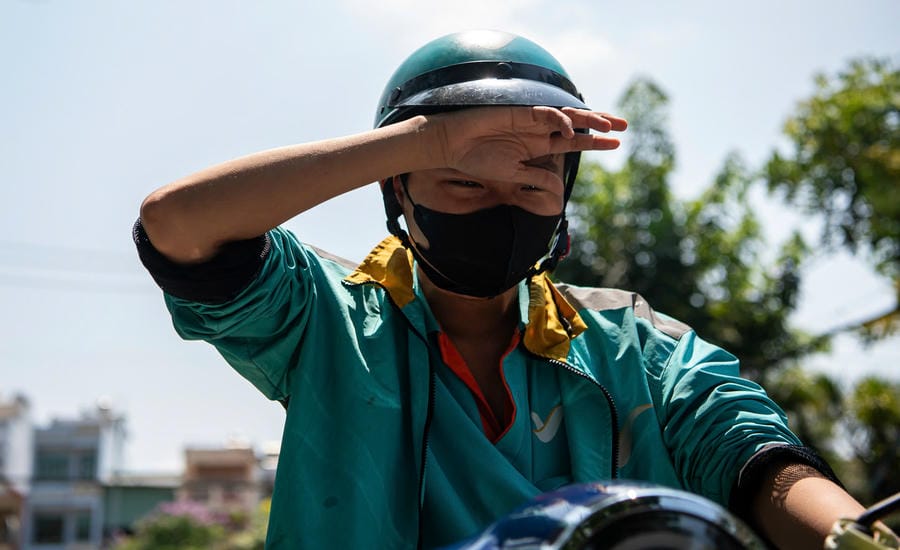 Bất chấp hơi nóng hầm hập phả lên từ mặt nhựa, một tài xế xe ôm công nghệ rớt những giọt mồ hôi nhọc nhằn để kịp giao bữa trưa cho khách. Ảnh: Anh Tú