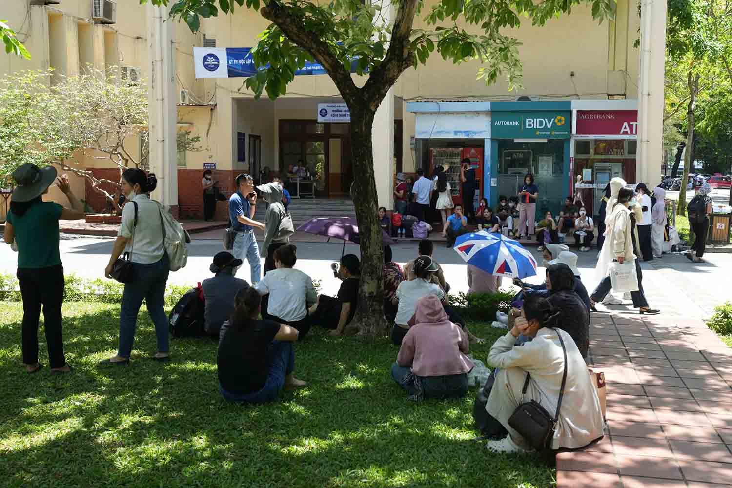 Nhiều phụ huynh ngồi dưới tán cây chờ sĩ tử hoàn thành bài thi đánh giá năng lực. Ảnh: Sóng Hữu 