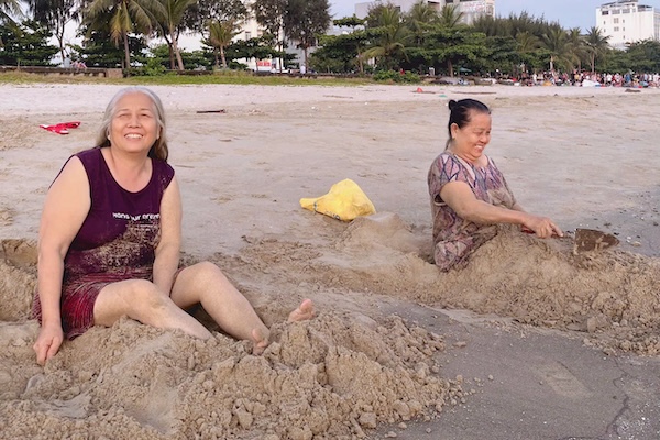 Bà Lợi ( người bên phải) giữ thói quen đắp cát mỗi buổi sáng để cải thiện đau chân. Ảnh: Ngọc Oanh.