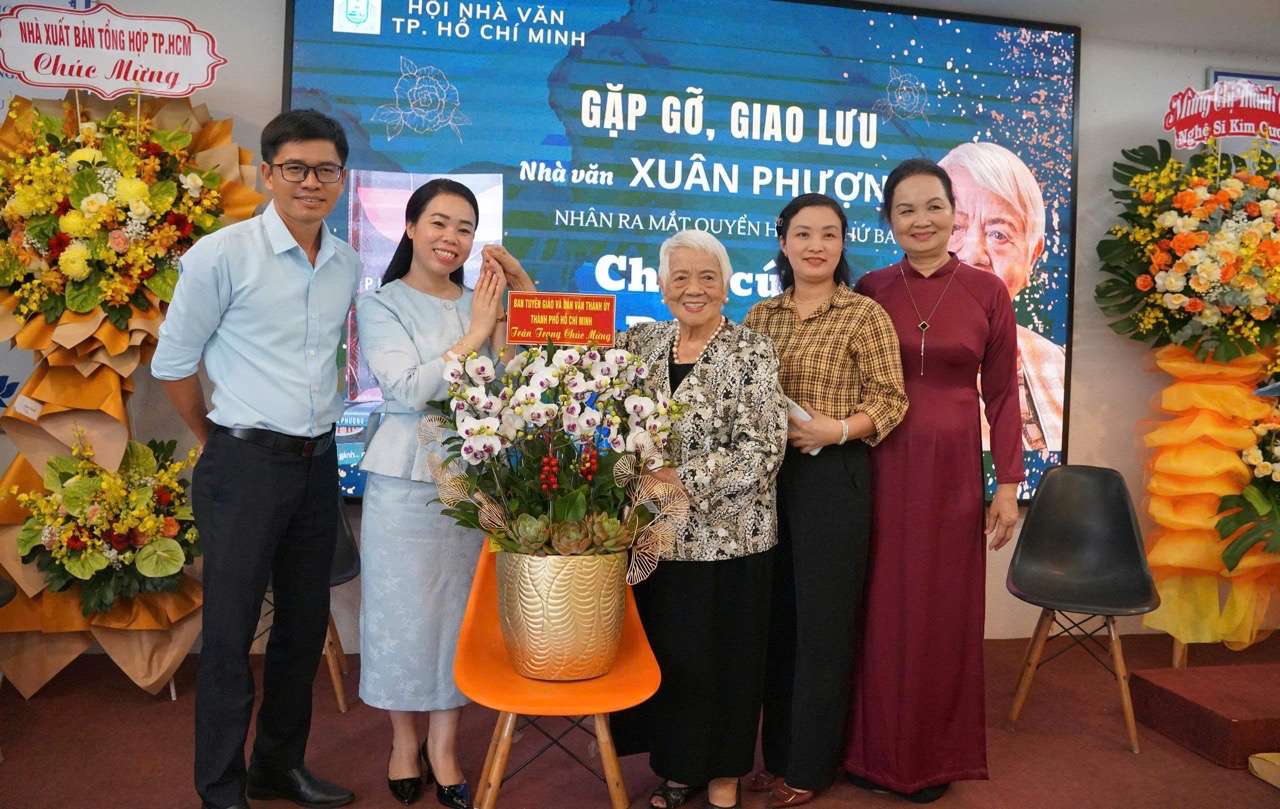 Bà Nguyễn Thị Kim Nguyên, Phó Ban Tuyên giáo và Dân vận Thành ủy TPHCM (thứ 2, trái qua) tặng hoa của Ban chúc mừng nhà văn Xuân Phượng. Ảnh: Mai Anh.