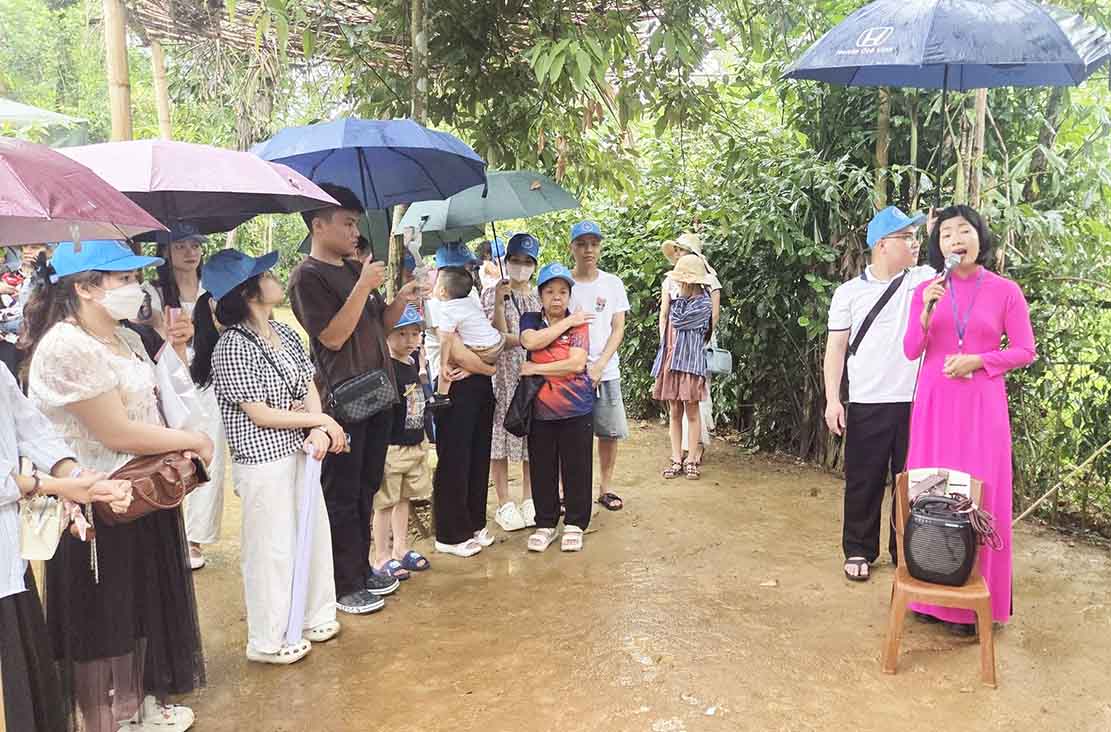 Du khách đội mưa nghe hướng dẫn viên thuyết minh về di tích. Ảnh: Mai Ngân