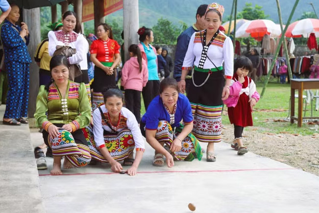 Phụ nữ Thái trong trang phục truyền thống tham gia chơi Tó mặng tại vạch xuất phát trong tư thế ngồi và quỳ bắn hạt mặng. Ảnh: Xuân Tiến/TTXVN