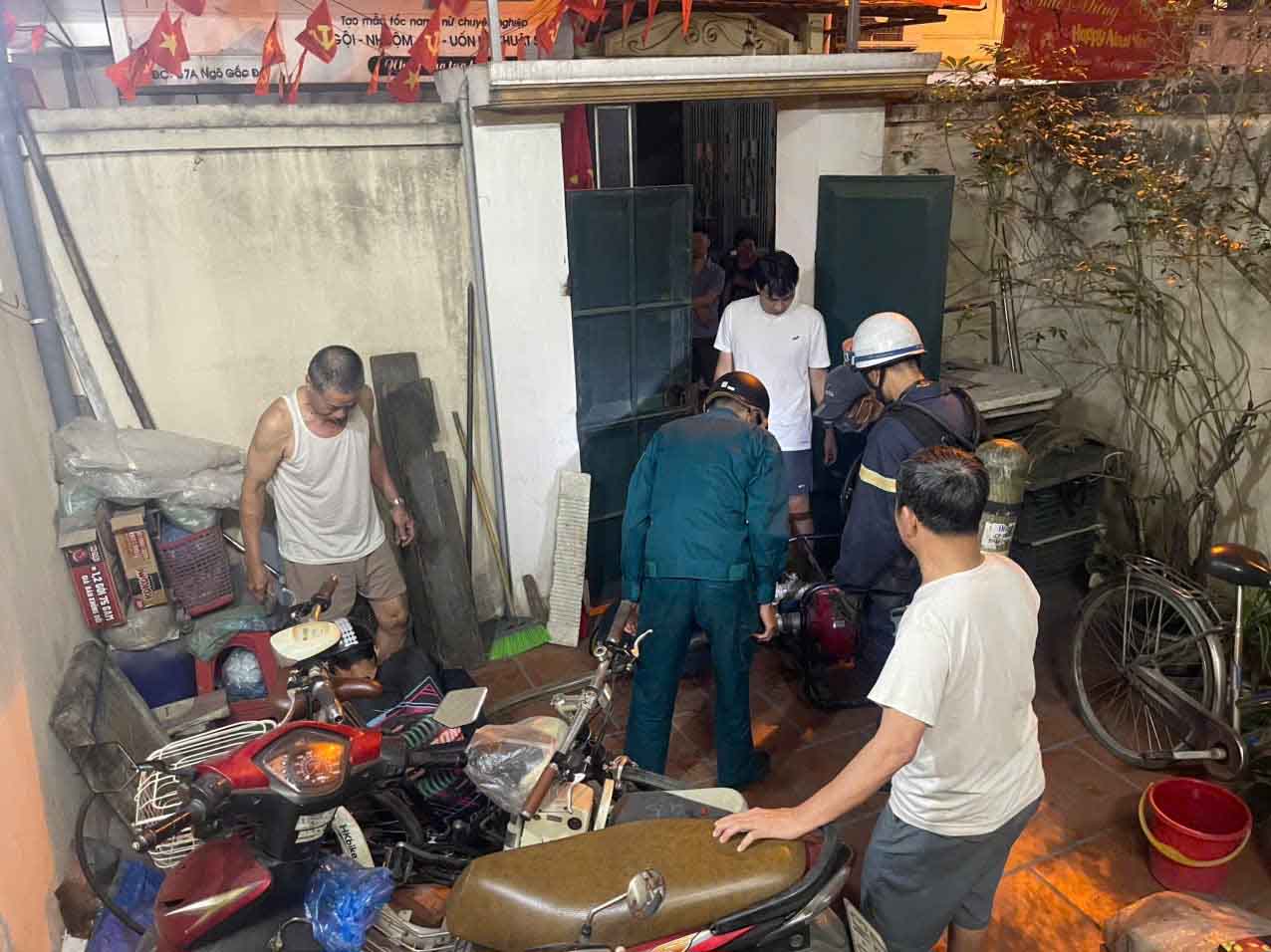 Lực lượng chức năng triển khai máy bơm khiêng tay hút nước từ bề ngầm của nhà dân bên cạnh để chữa cháy. Ảnh: Công an Hà Nội 