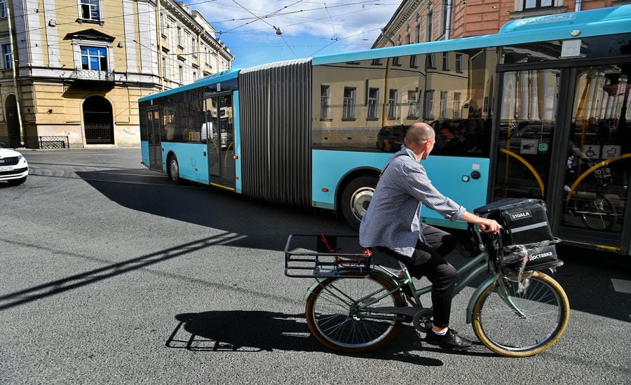 Một người đàn ông đi xe đạp băng qua đường cạnh chiếc xe buýt tại Saint Petersburg (Nga), khoảnh khắc giao cắt giữa phương tiện cá nhân và hệ thống giao thông công cộng. Ảnh: Việt Văn