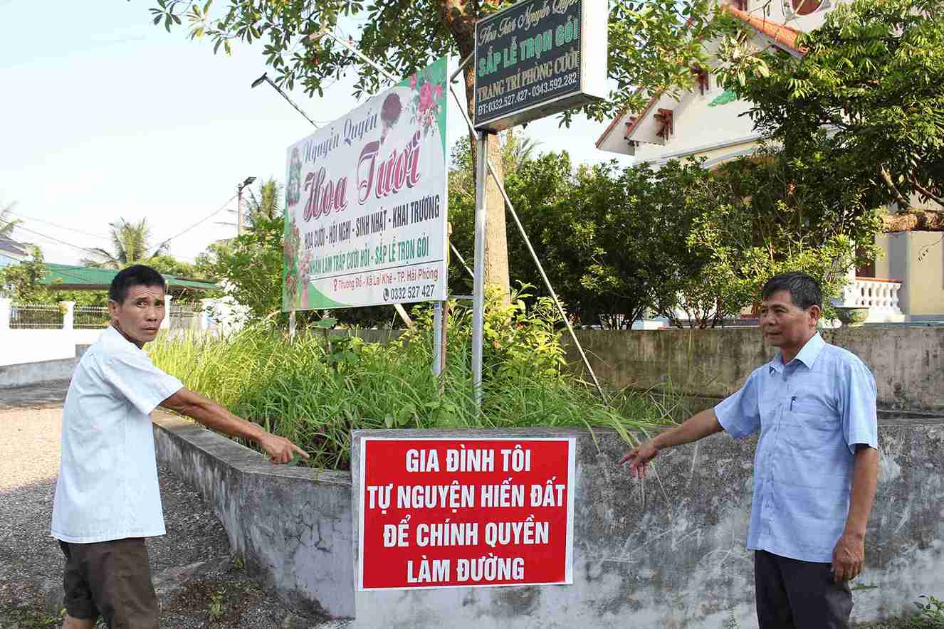Ông Tô Văn Quyết và ông Tạ Văn Hiến bên tấm biển tuyên truyền về phong trào hiến đất làm đường ở thôn Thượng Đỗ.